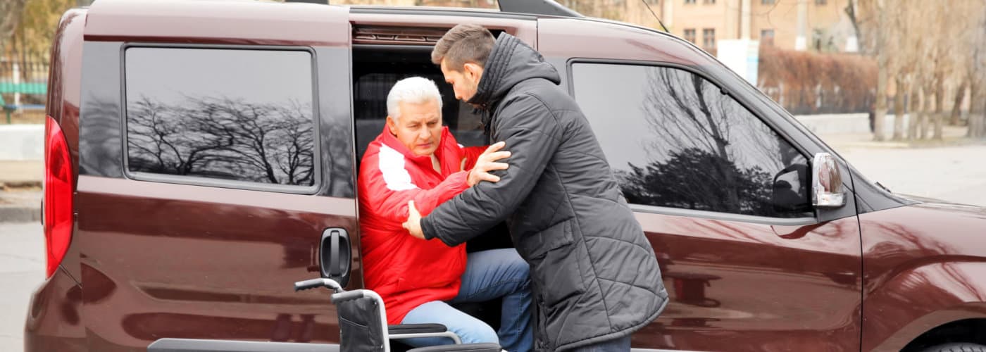 man assisting a senior man getting of a van