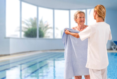 caregiver helping elderly woman to get out of swimming pool with bath towel