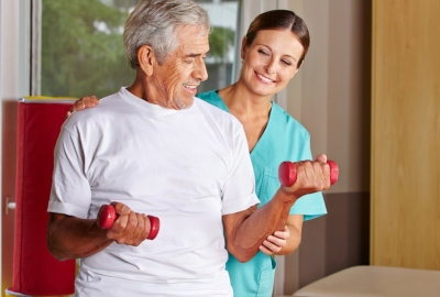senior man with dumbbells in rehab with a physiotherapist